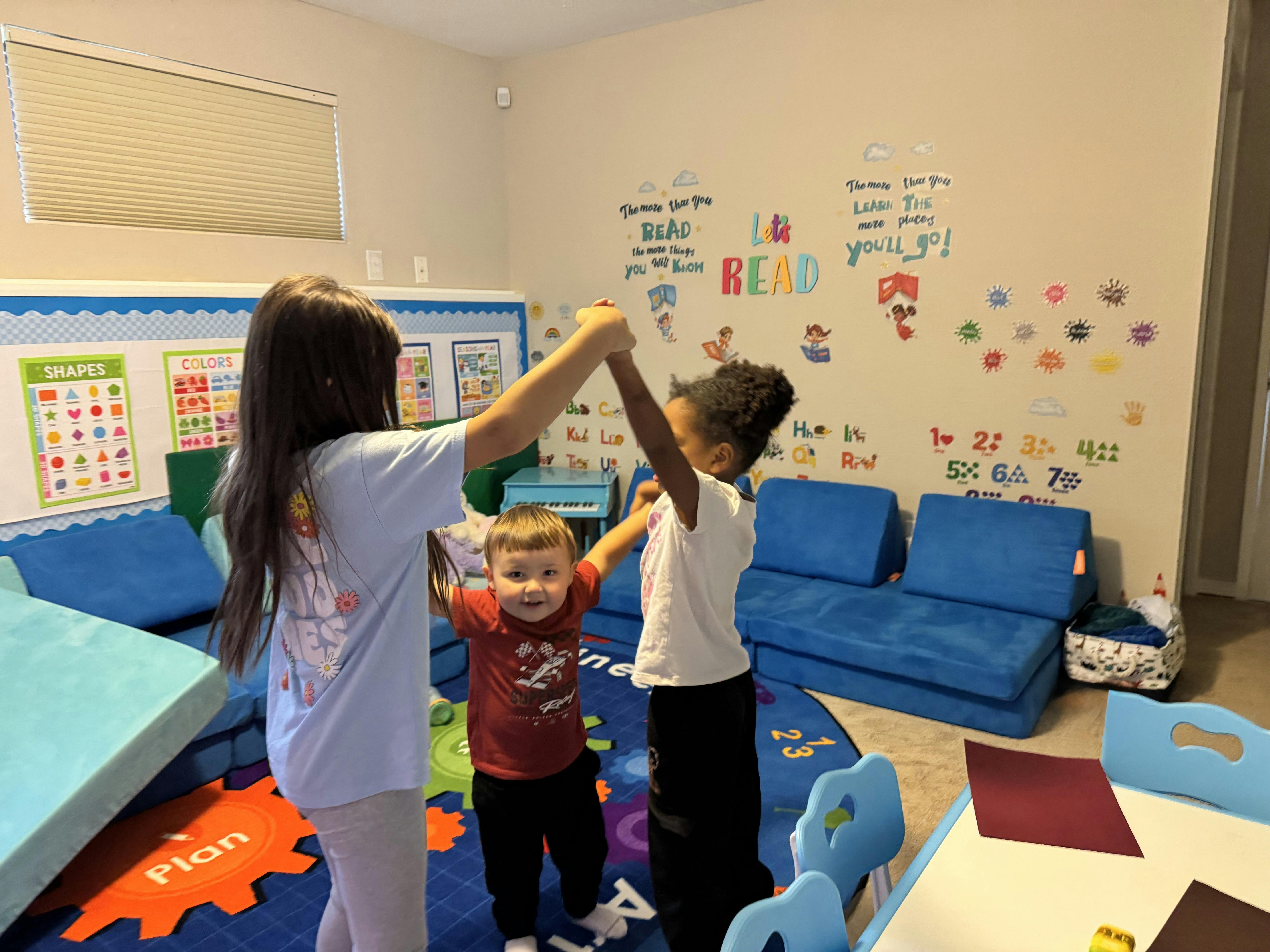 Three children holding hands in a circle in a classroom