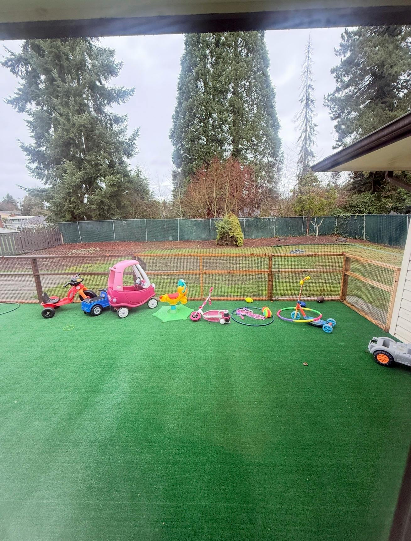 Children's toys on artificial turf, fenced yard and trees in background