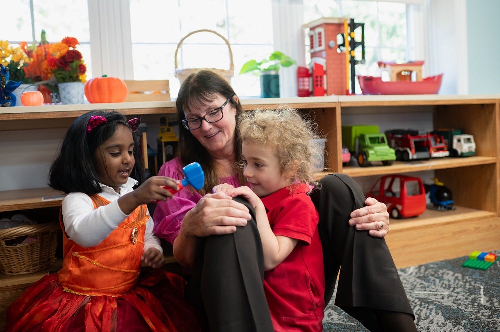 Adult and two children playing with toys in a classroom