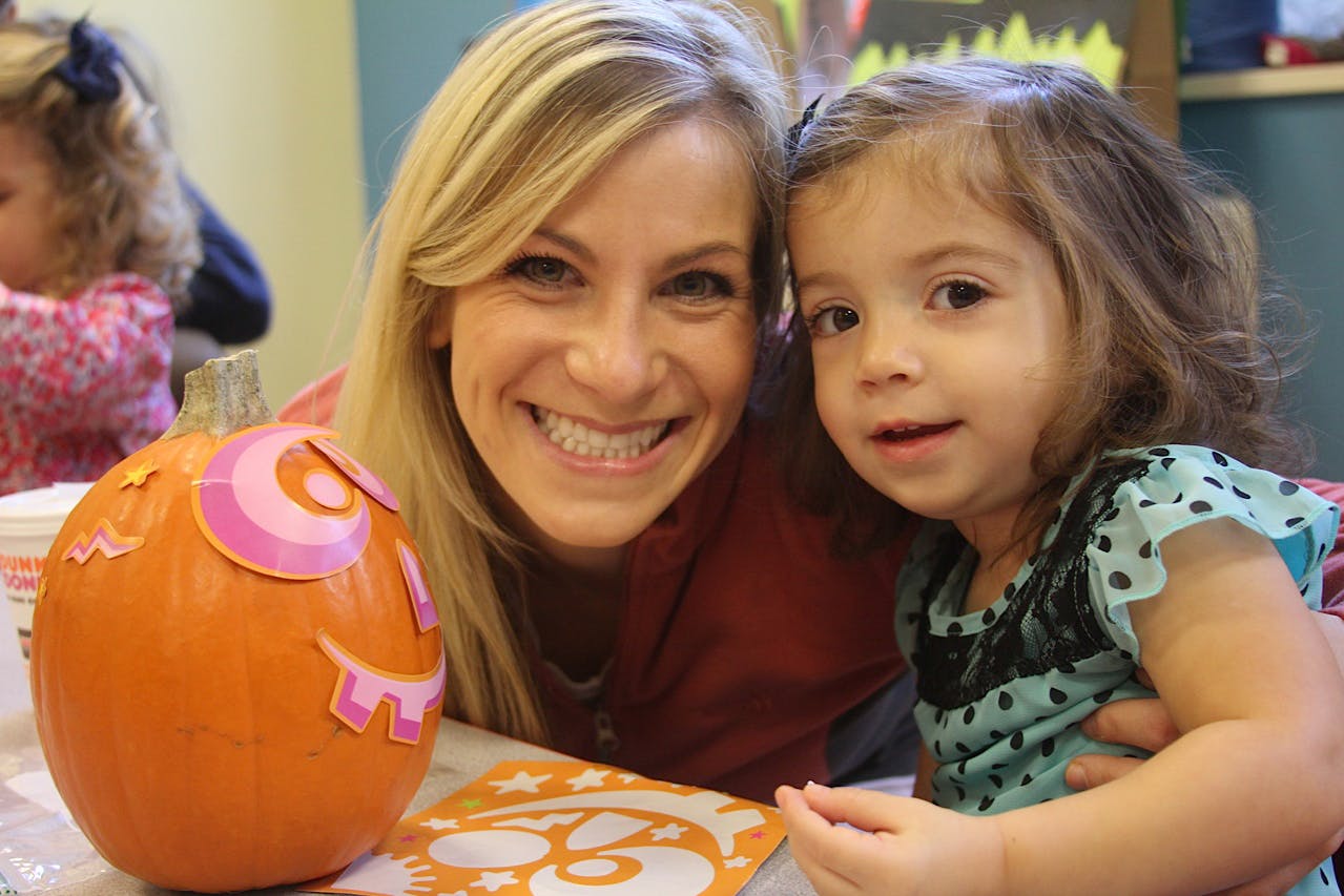 Person and child next to a decorated pumpkin