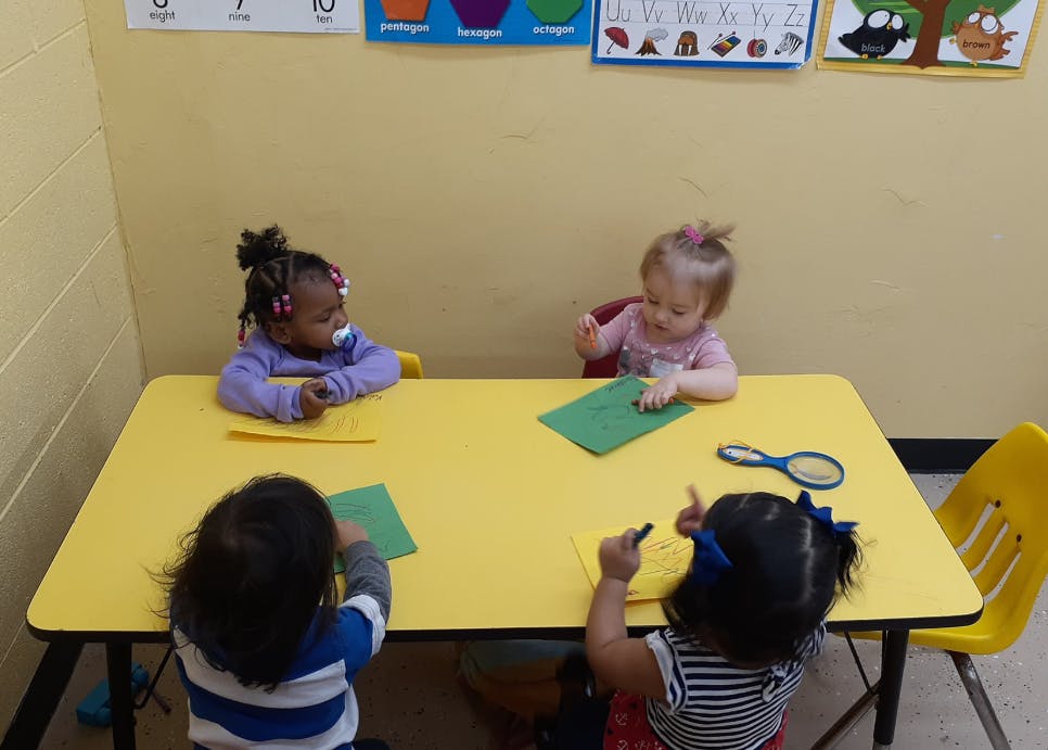 Four children sitting at a yellow table with paper