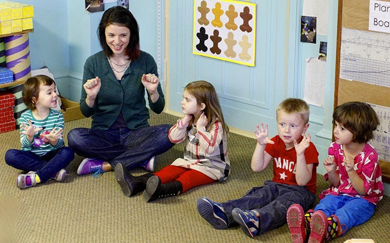 Adult and children sitting on floor, gesturing with adult leading an two children gesturing