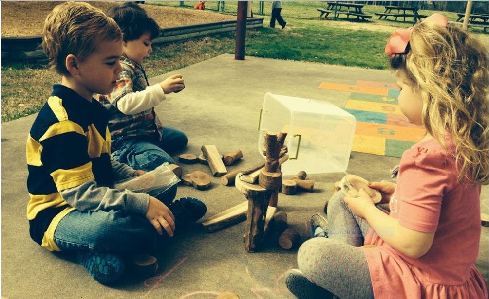 Three children playing with wooden blocks outdoors