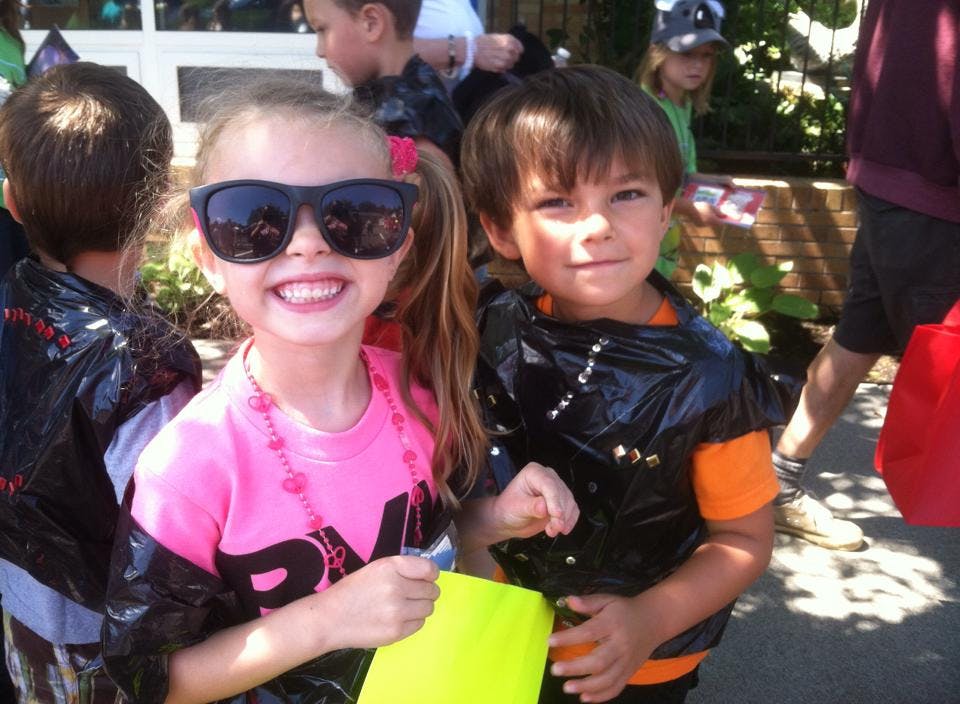 Two children in costumes, one wearing sunglasses, both wearing black plastic over clothes