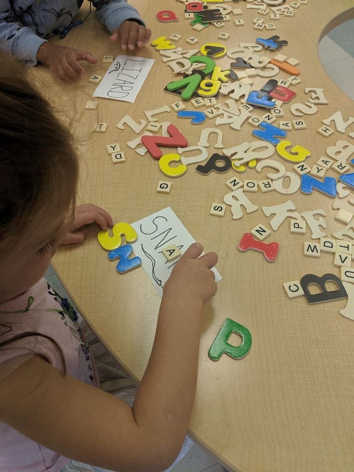 Child placing letter tiles on a paper with the word "SNAKE"