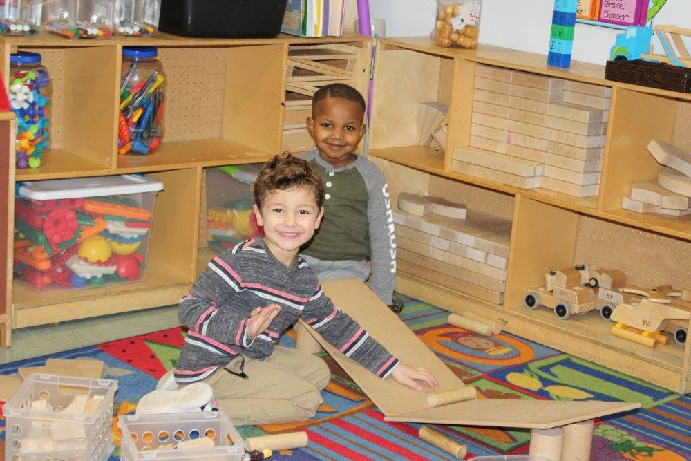 Two children playing with cardboard ramp and blocks in a classroom