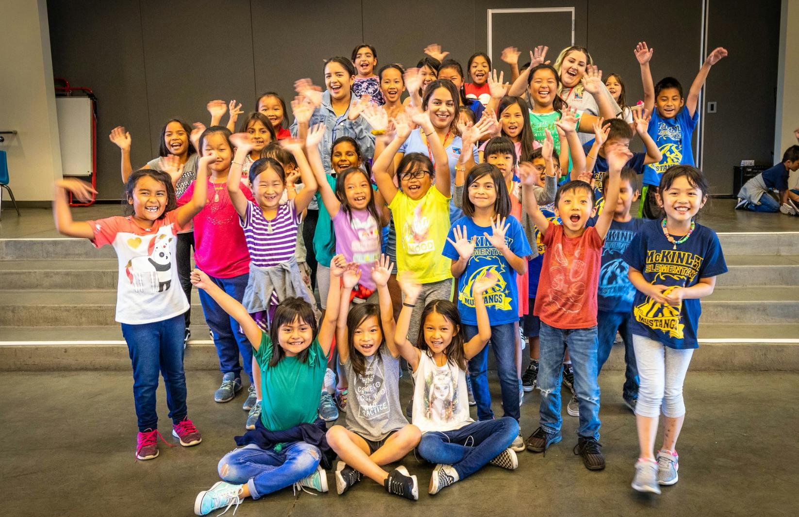 Large group of adults and children waving and smiling
