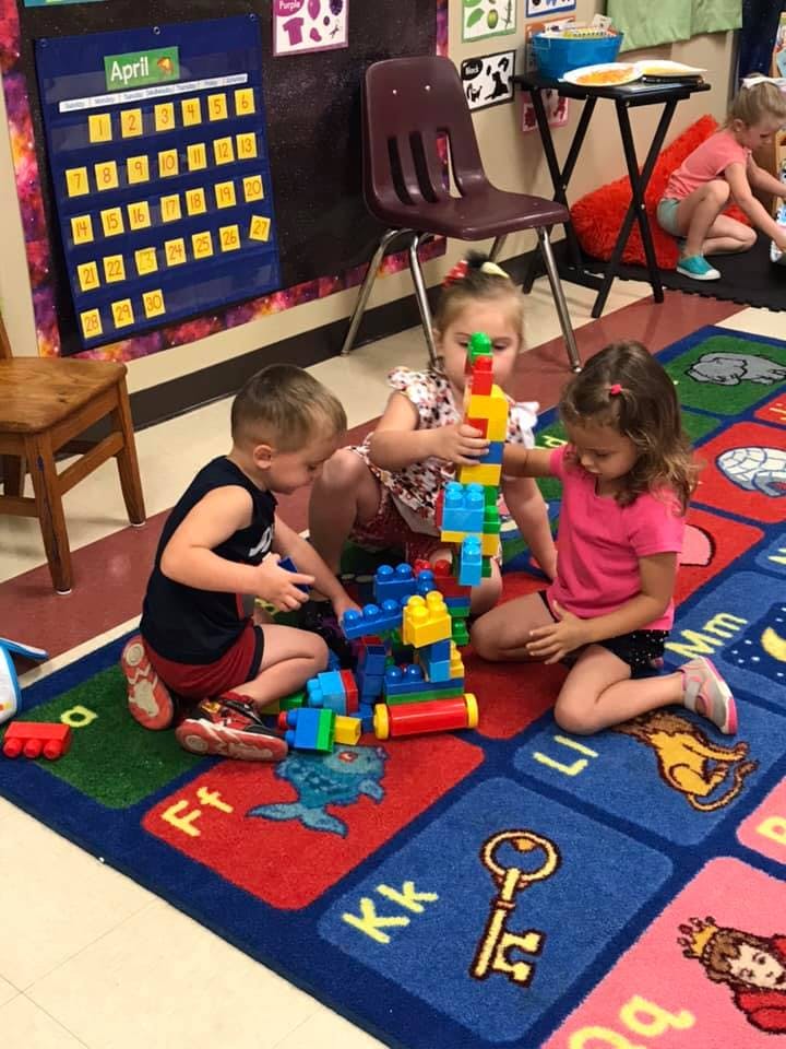 Three children playing with colorful building blocks on a rug