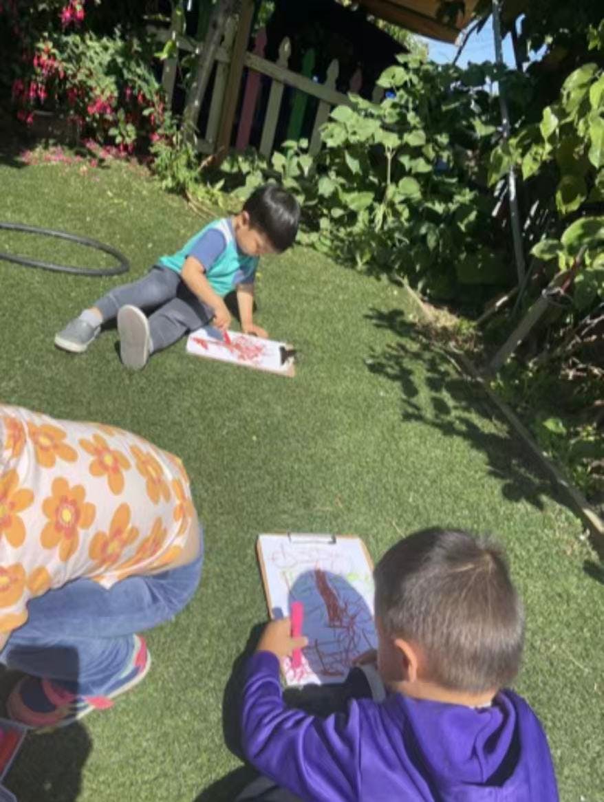 Children sitting on grass using clipboards to draw with markers
