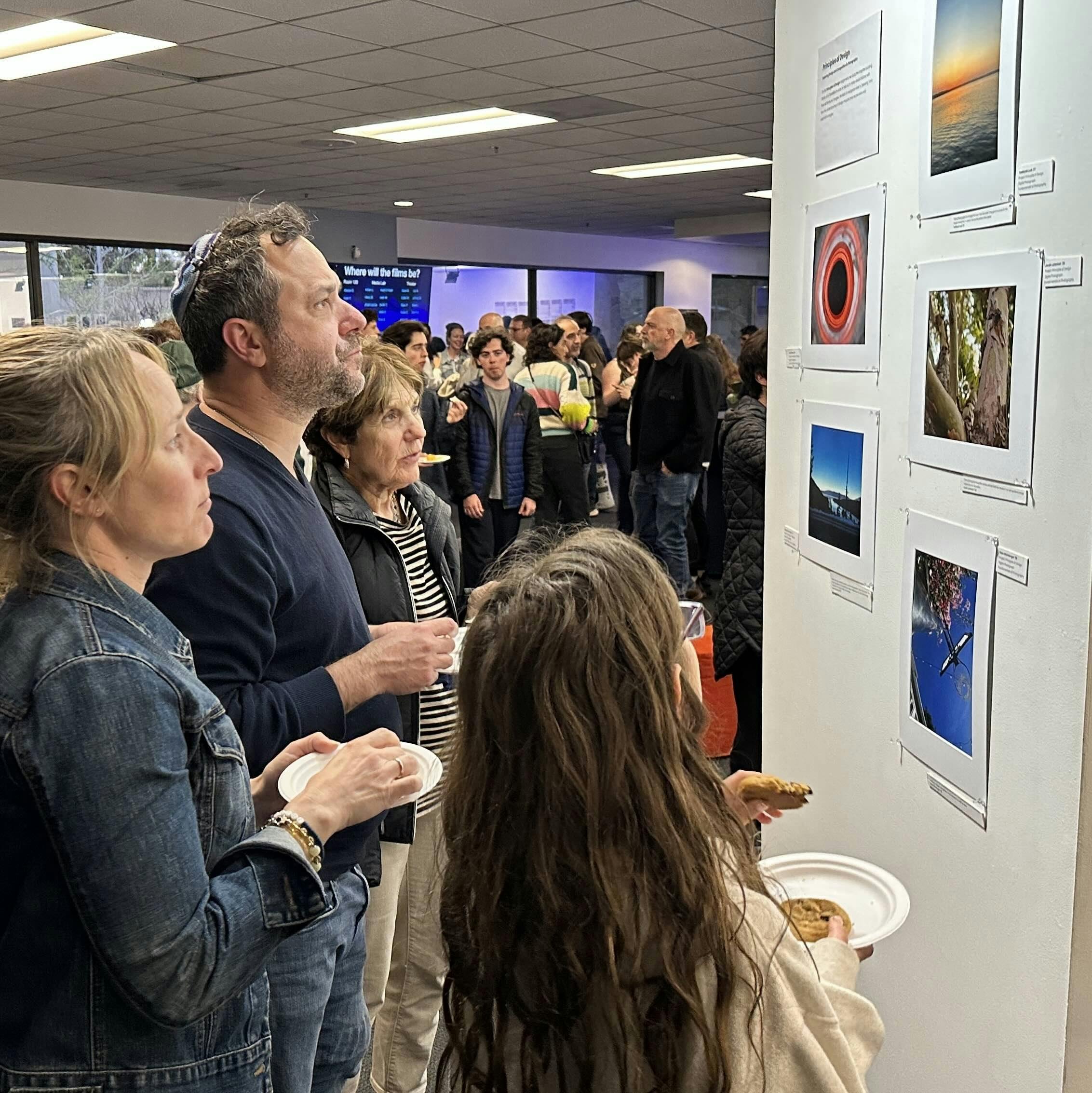 People holding plates and looking at photos displayed on a wall