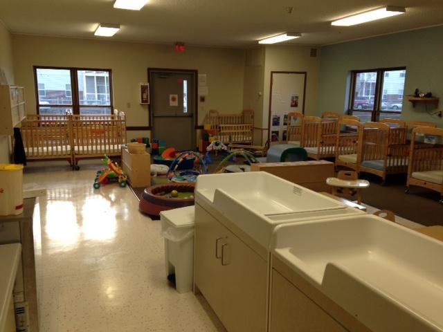 Empty infant daycare room with many cribs and changing stations