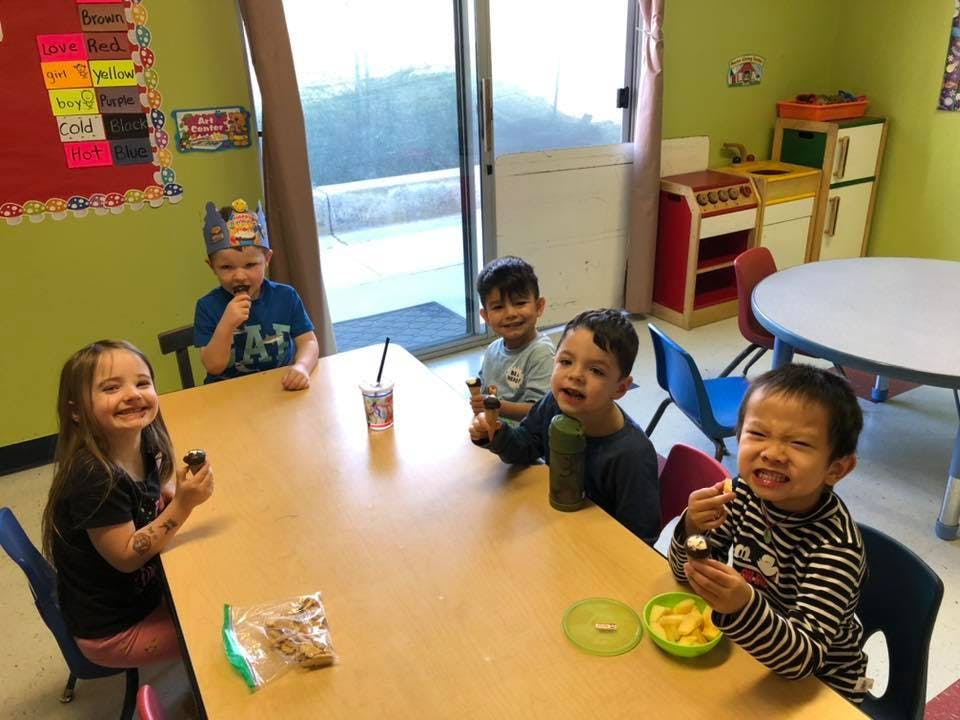 Children sitting at a table eating snacks in a classroom