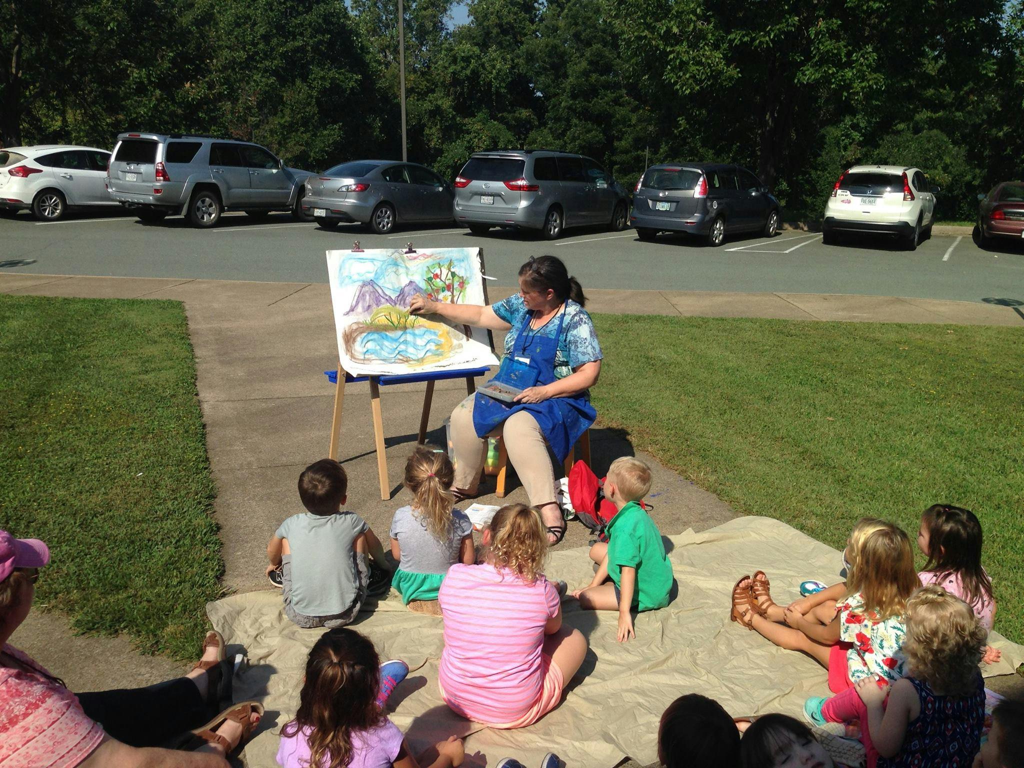Person reading to a group of children outdoors