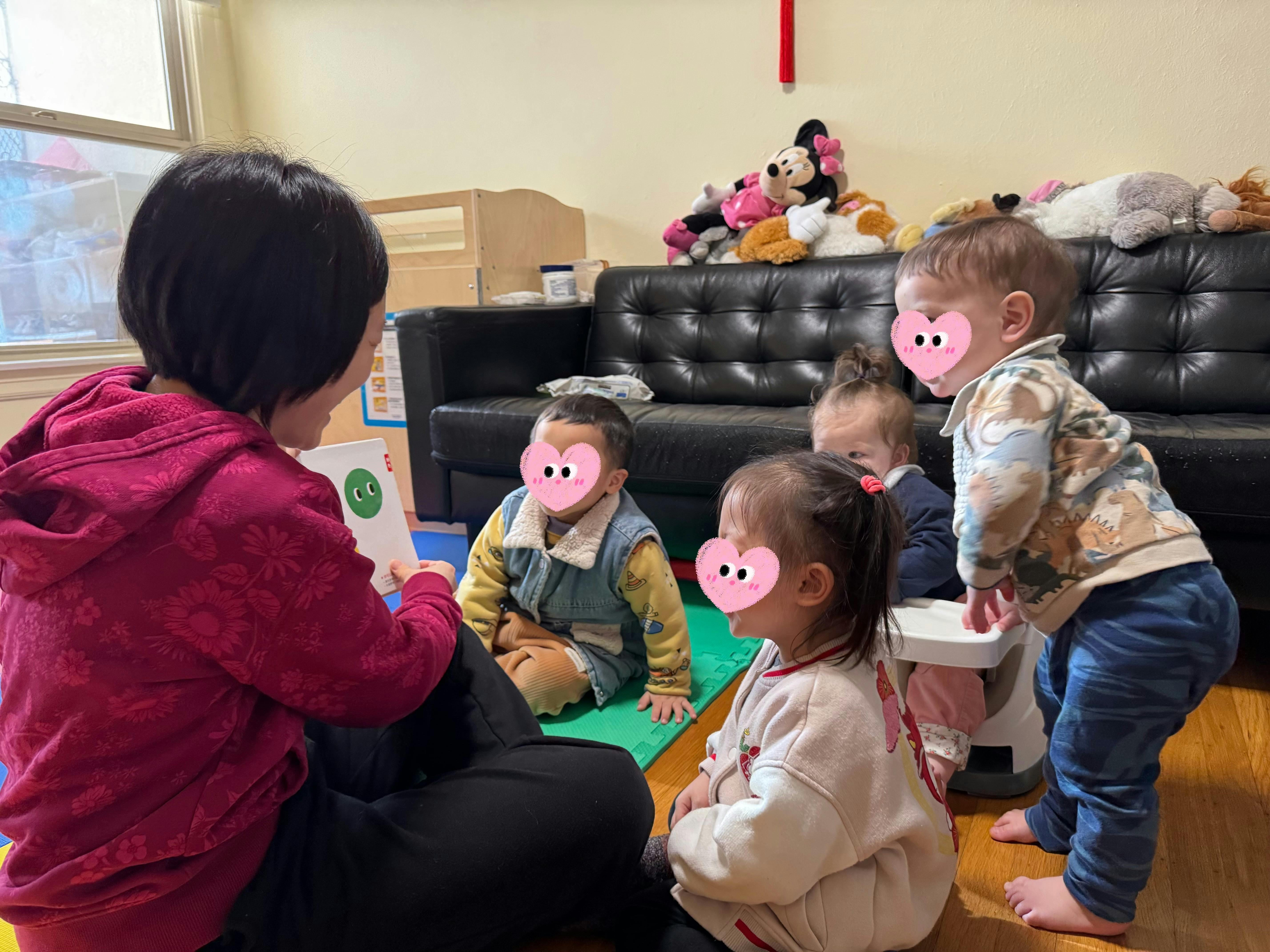 Person reading a book to four young children sitting on the floor
