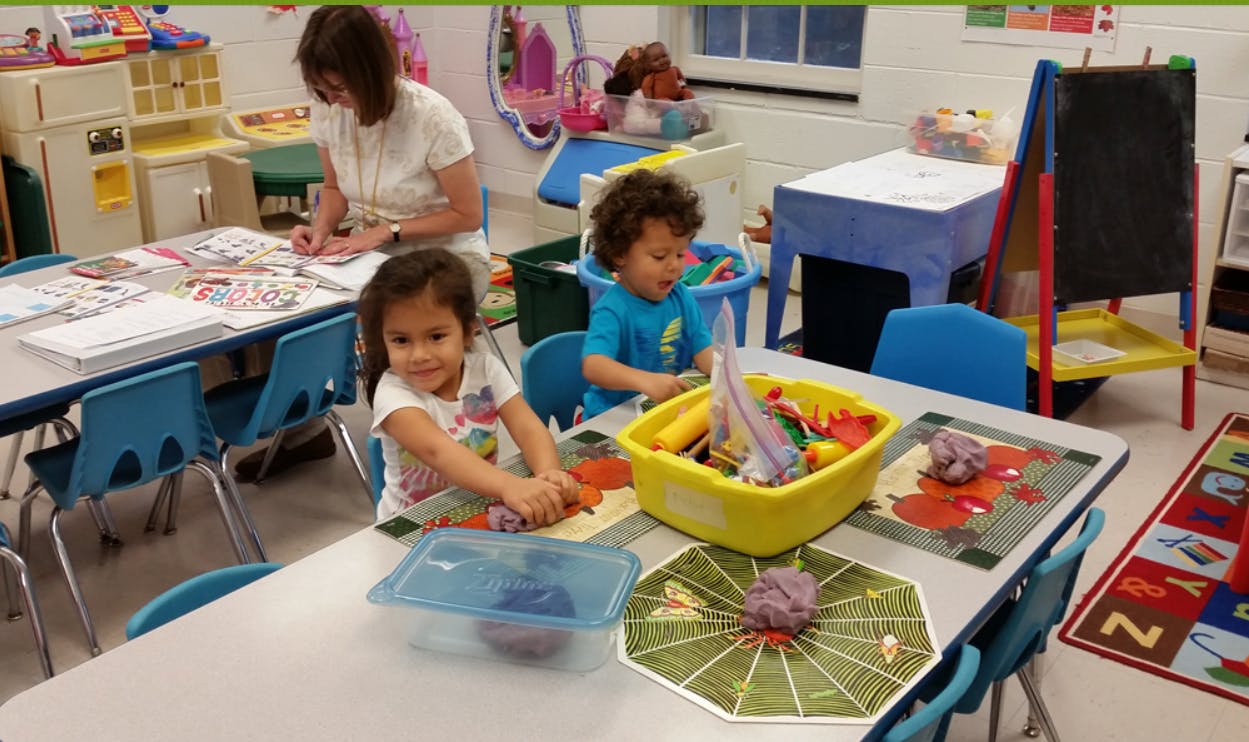 Adult and two children at tables in a classroom