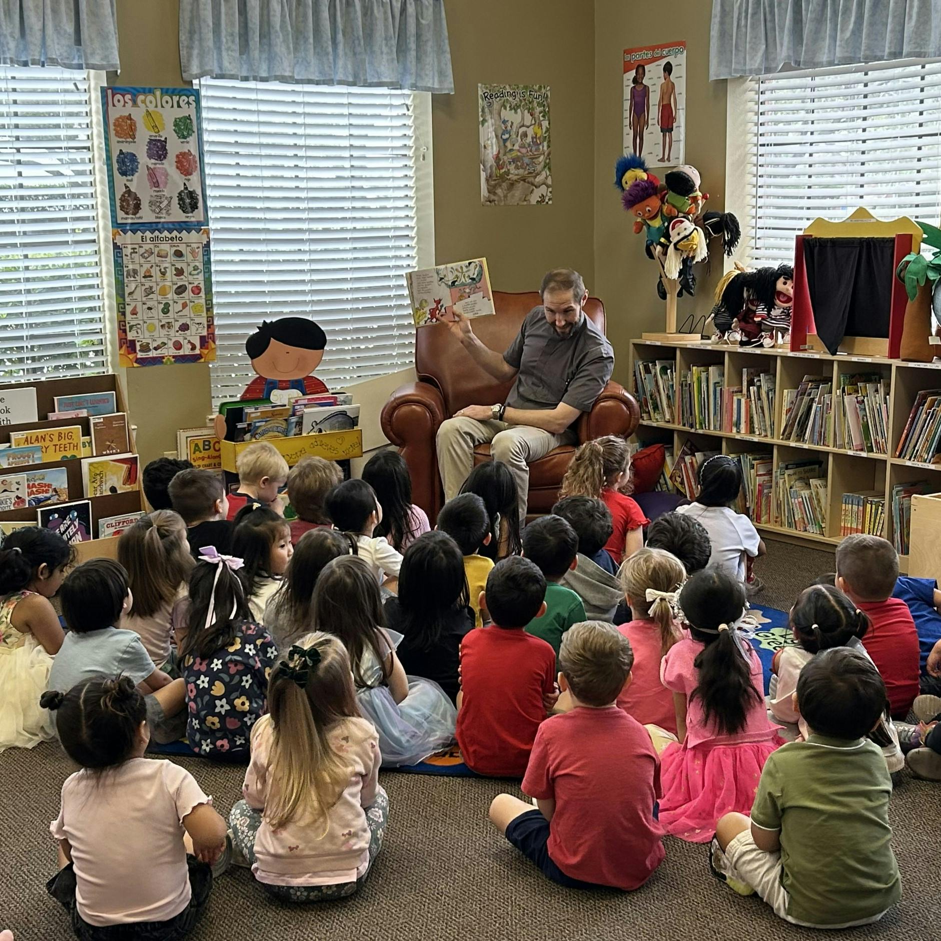 Man reading a book to a group of children in a classroom