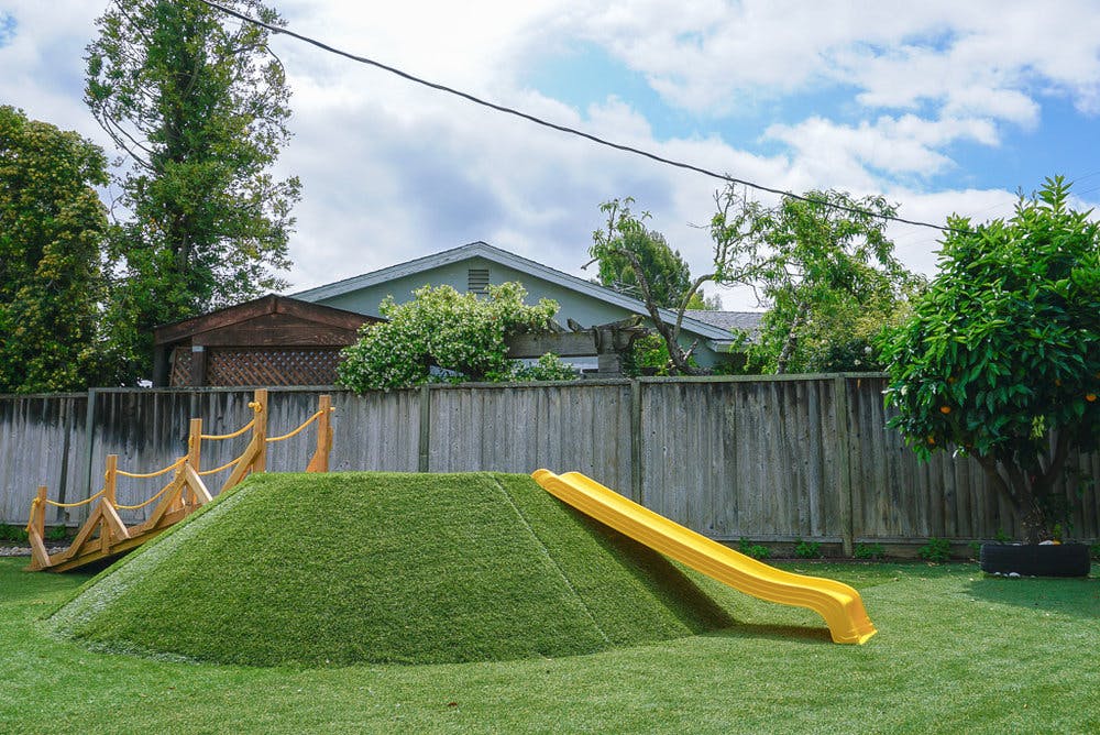 Grassy mound with a yellow slide and a rope climbing structure