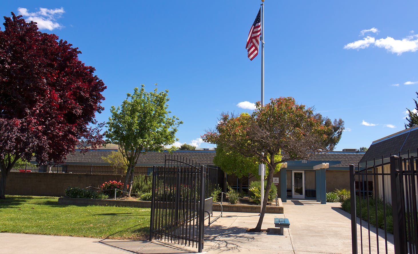American flag on a pole in front of a building with trees and a fence
