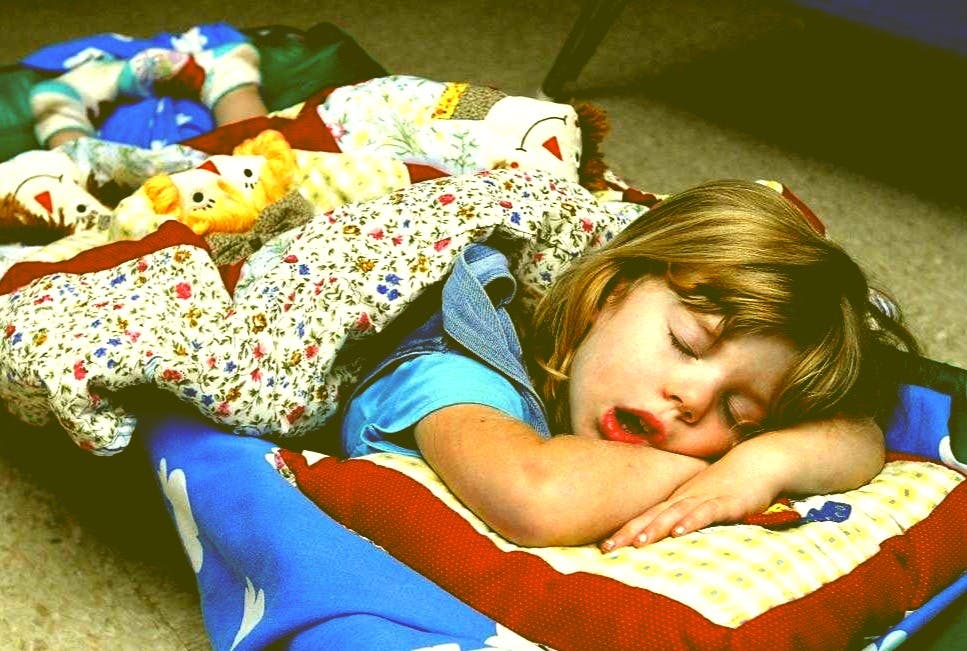 Child sleeping on a mat with a pillow and blanket