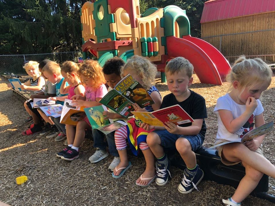 Children sitting on a bench reading books on a playground