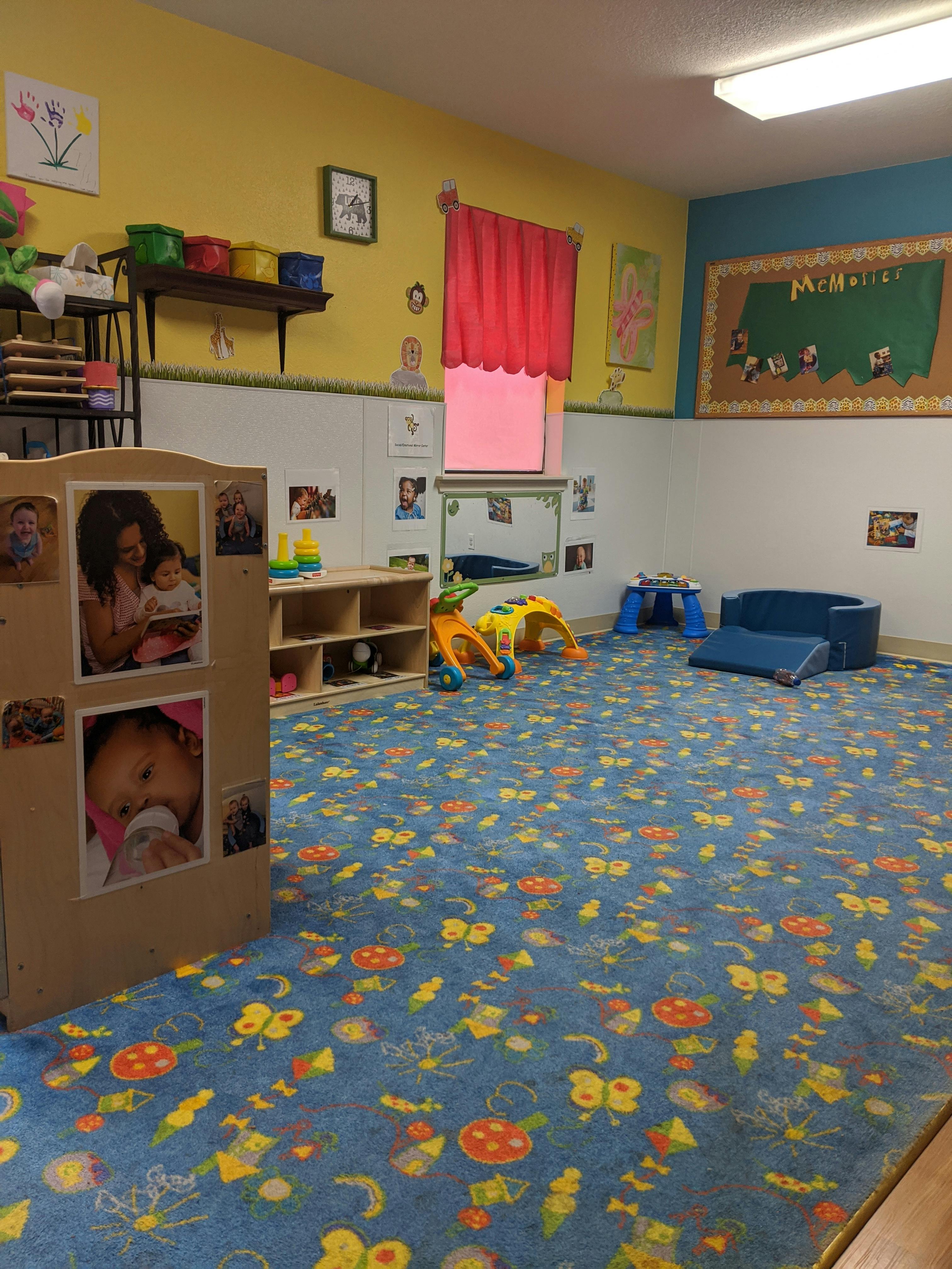 Playroom with blue patterned carpet, shelves, and small play equipment