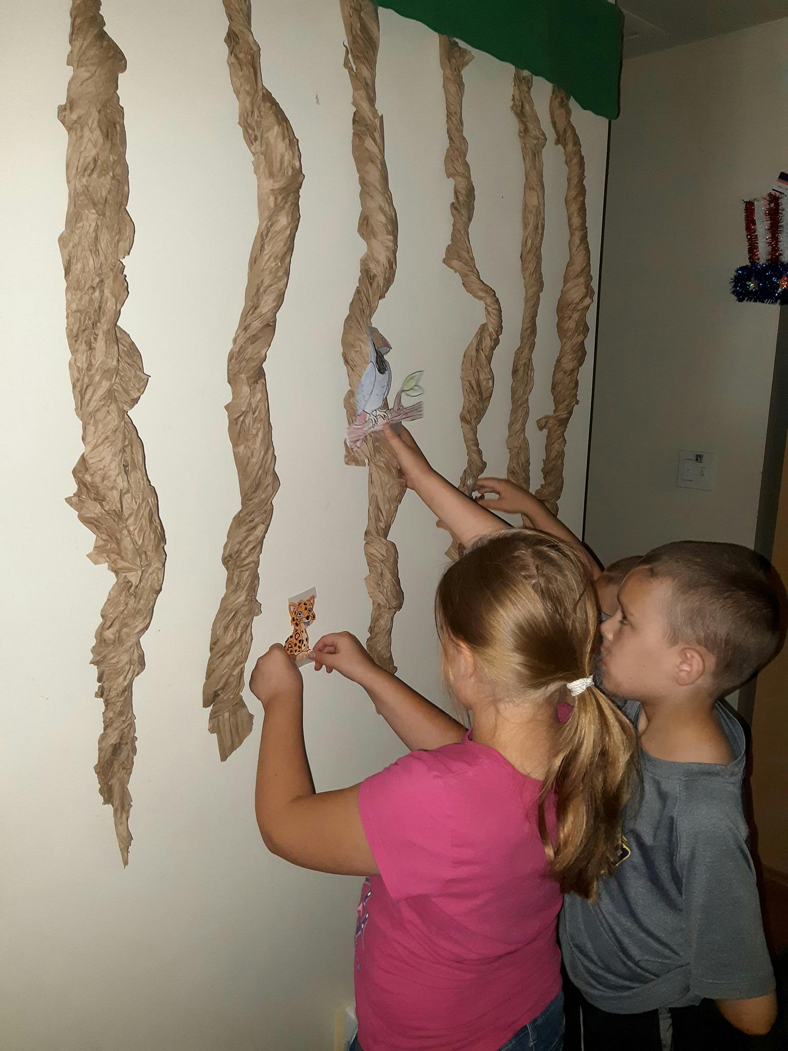 Two children placing decorations on a wall with brown paper vines