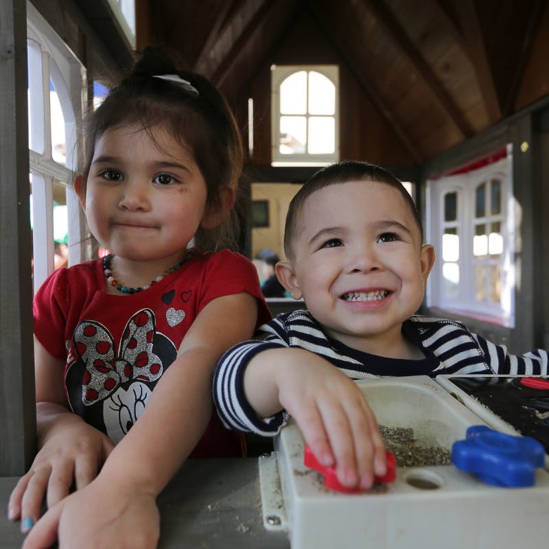 Two children in a playhouse, one child playing with a toy