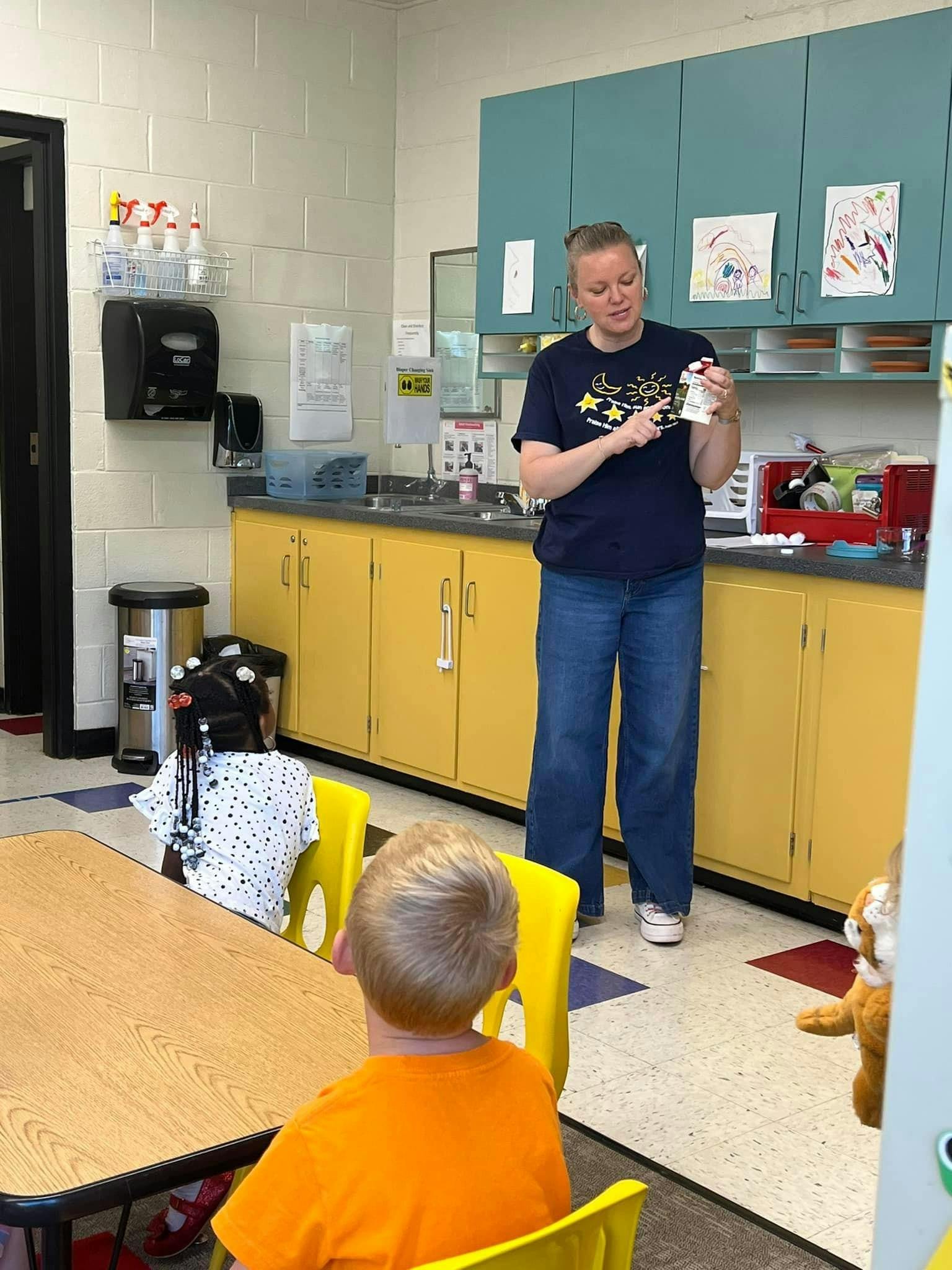 Person standing in a classroom holding an object and pointing at it