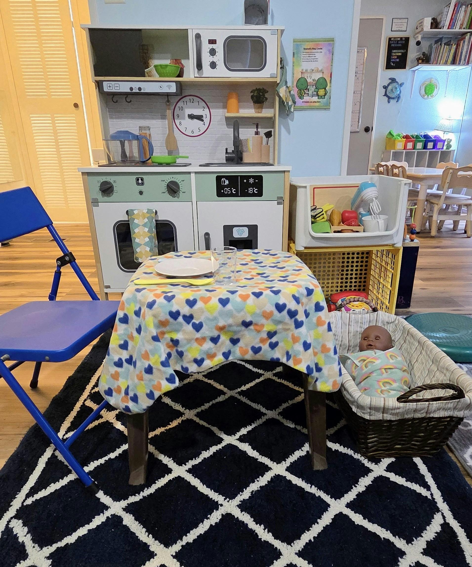 Doll in a basket, table with a heart-patterned cloth, and a toy kitchen playset