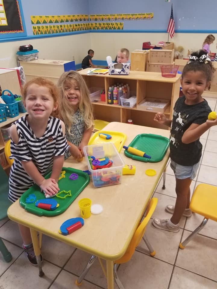 Three children playing with modeling clay at a table in a classroom