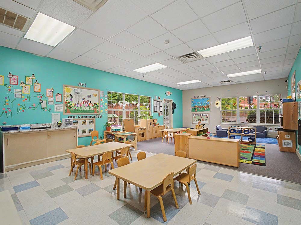 A colorful classroom with small tables and chairs, bright walls, and large windows