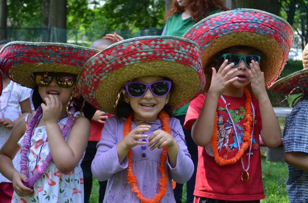 Three children wearing sombreros, sunglasses, and leis