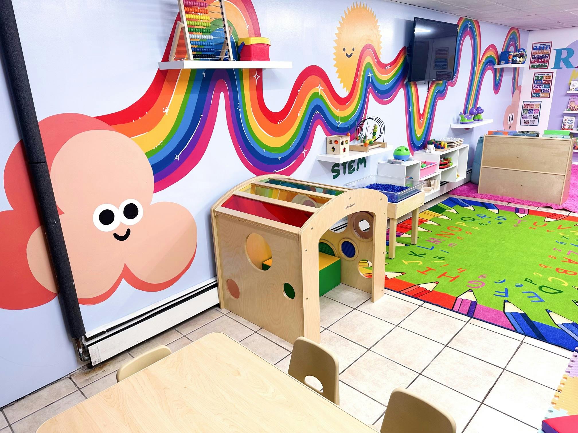 Playroom with rainbow wall art, play structure, and small tables