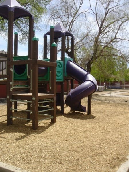 Playground structure with a purple slide and wood chip ground
