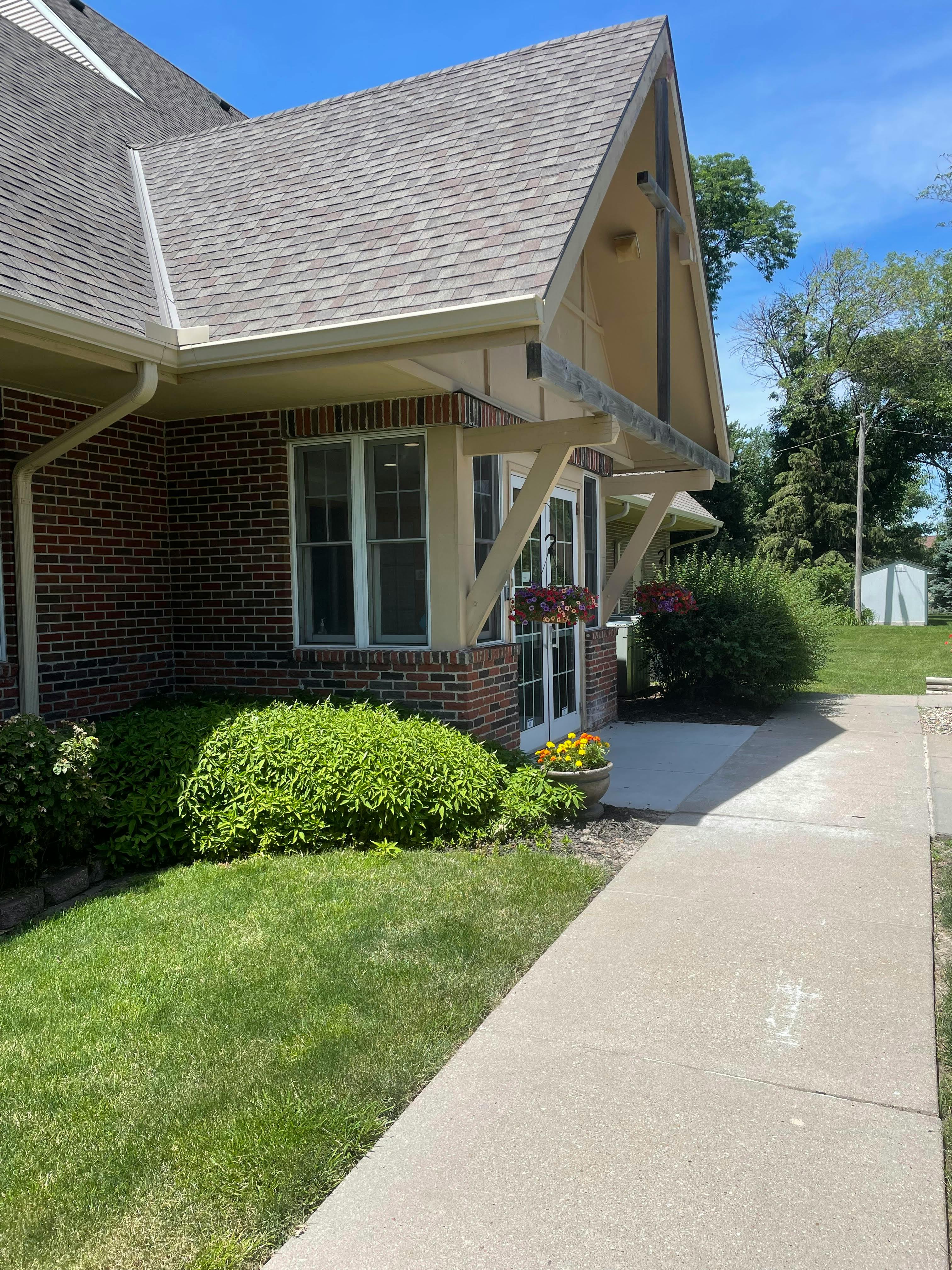 Side of a brick building with a peaked roof and a sidewalk
