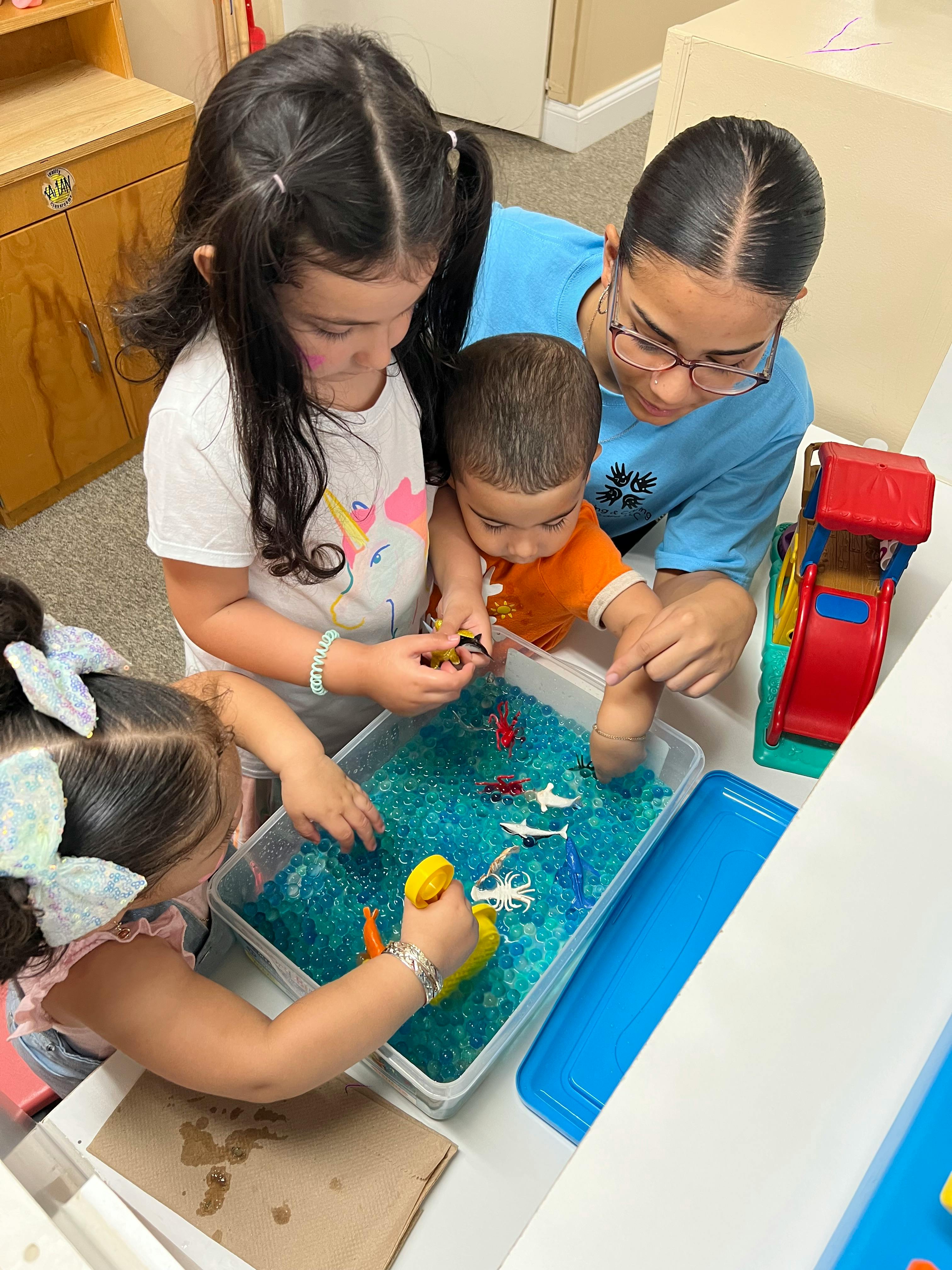 Adult and children playing with water beads and toys in a sensory bin