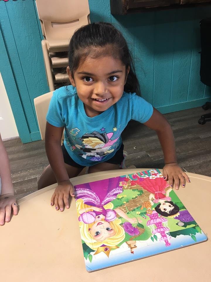 Child kneeling at a table with a puzzle