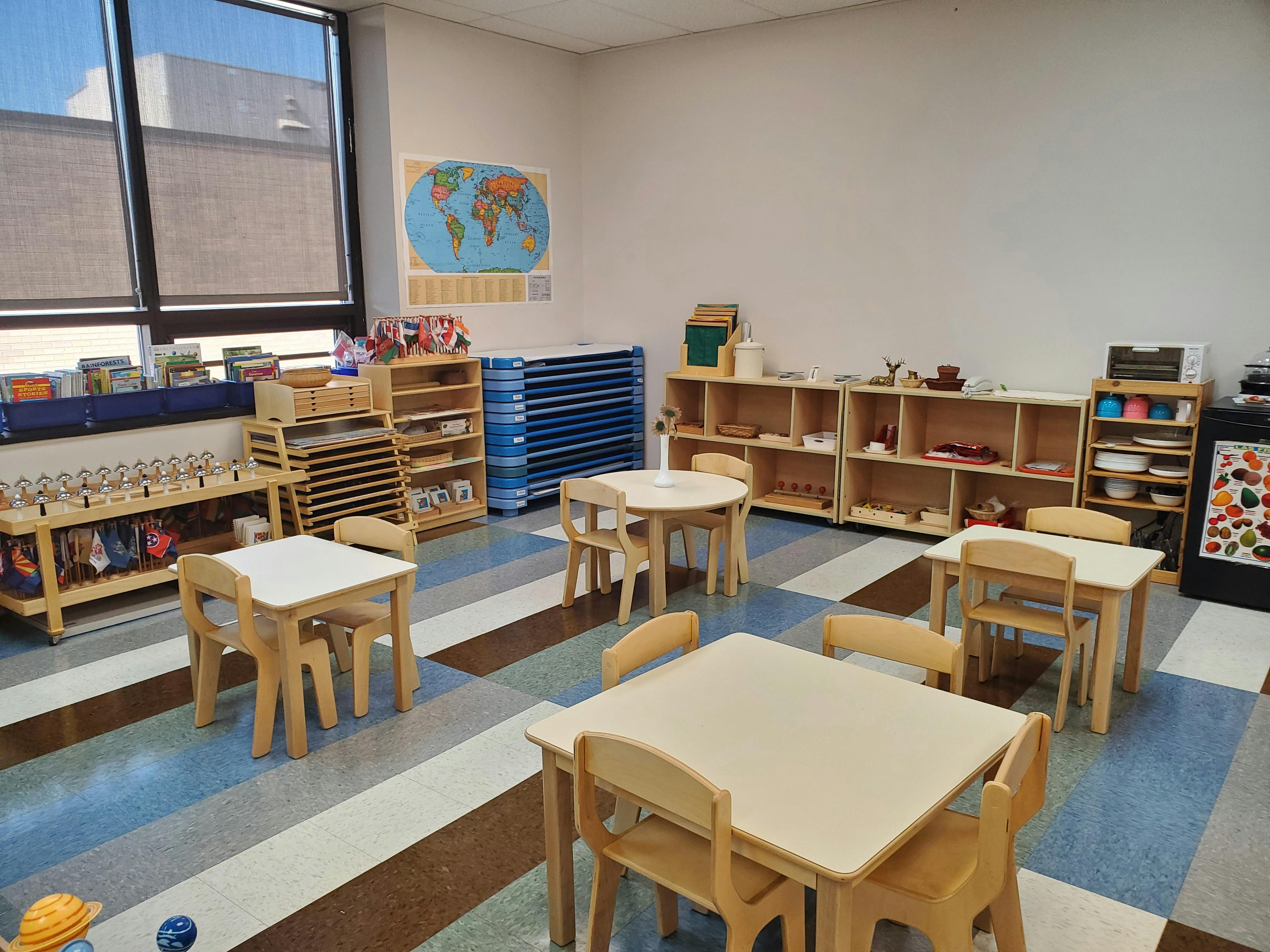 Empty classroom with small tables and chairs, shelves with learning materials