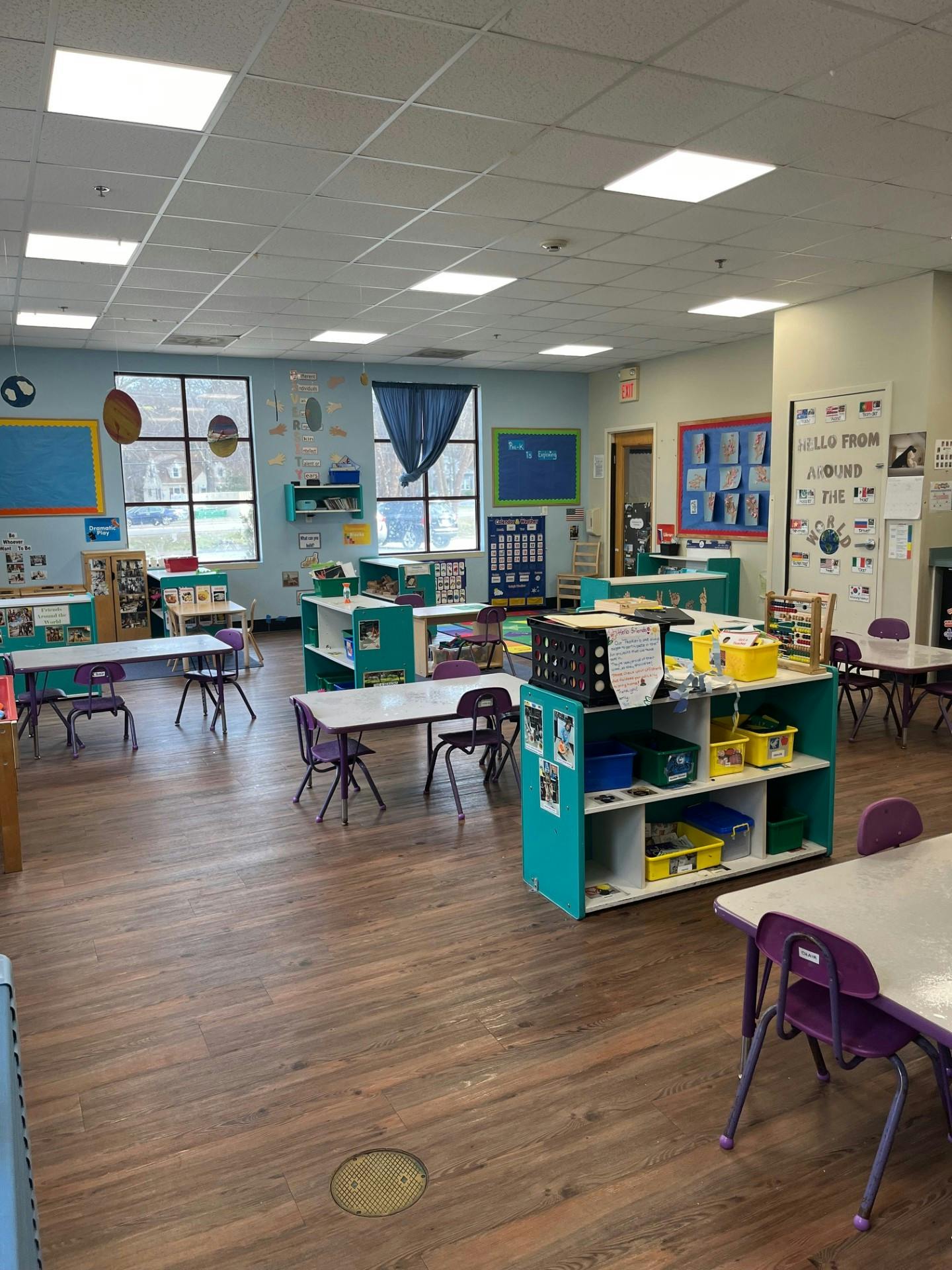 An empty classroom with small tables and chairs, and learning materials on shelves