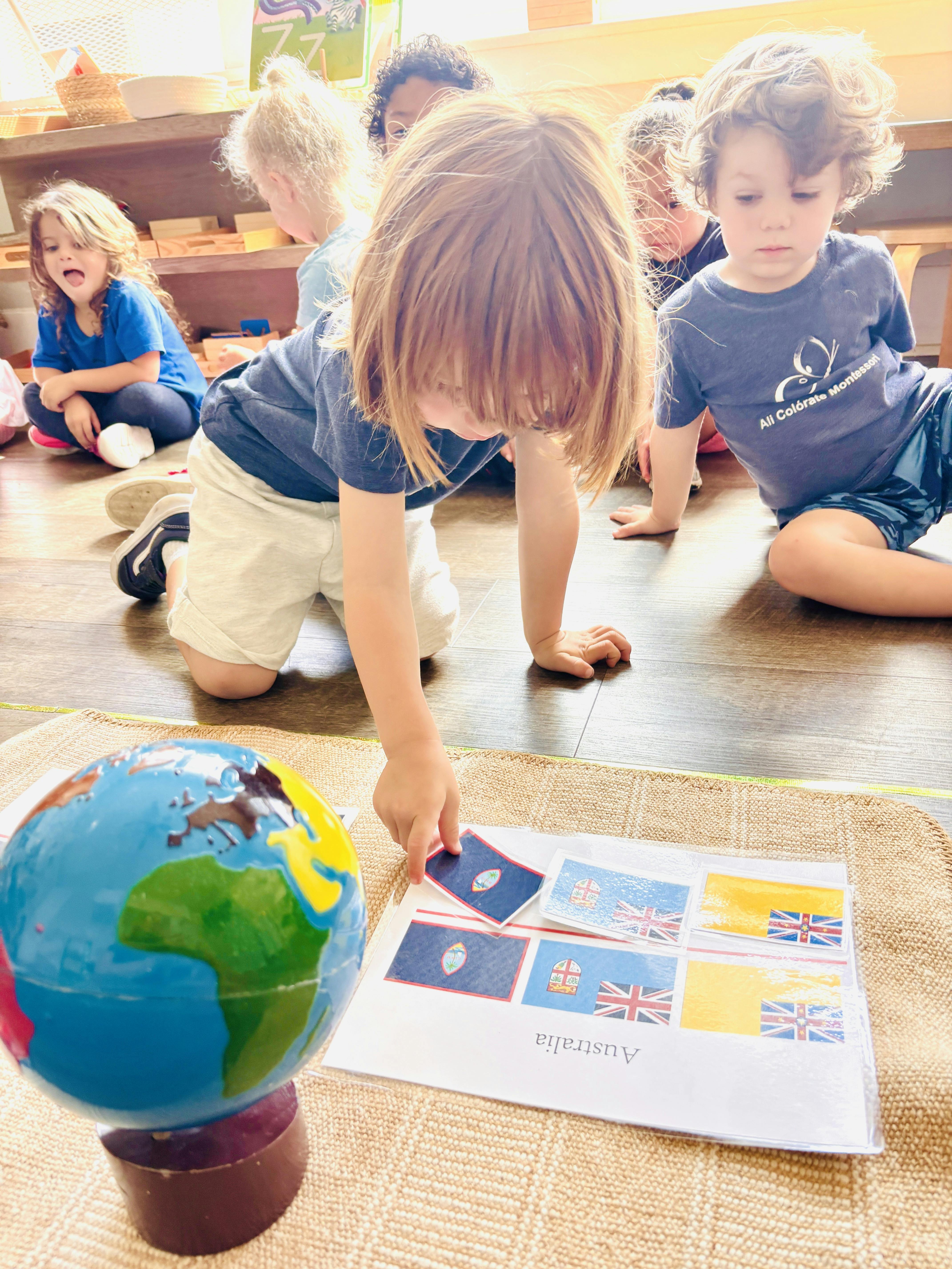Child kneeling on floor, selecting a flag card next to a globe and “Australia” labeled page