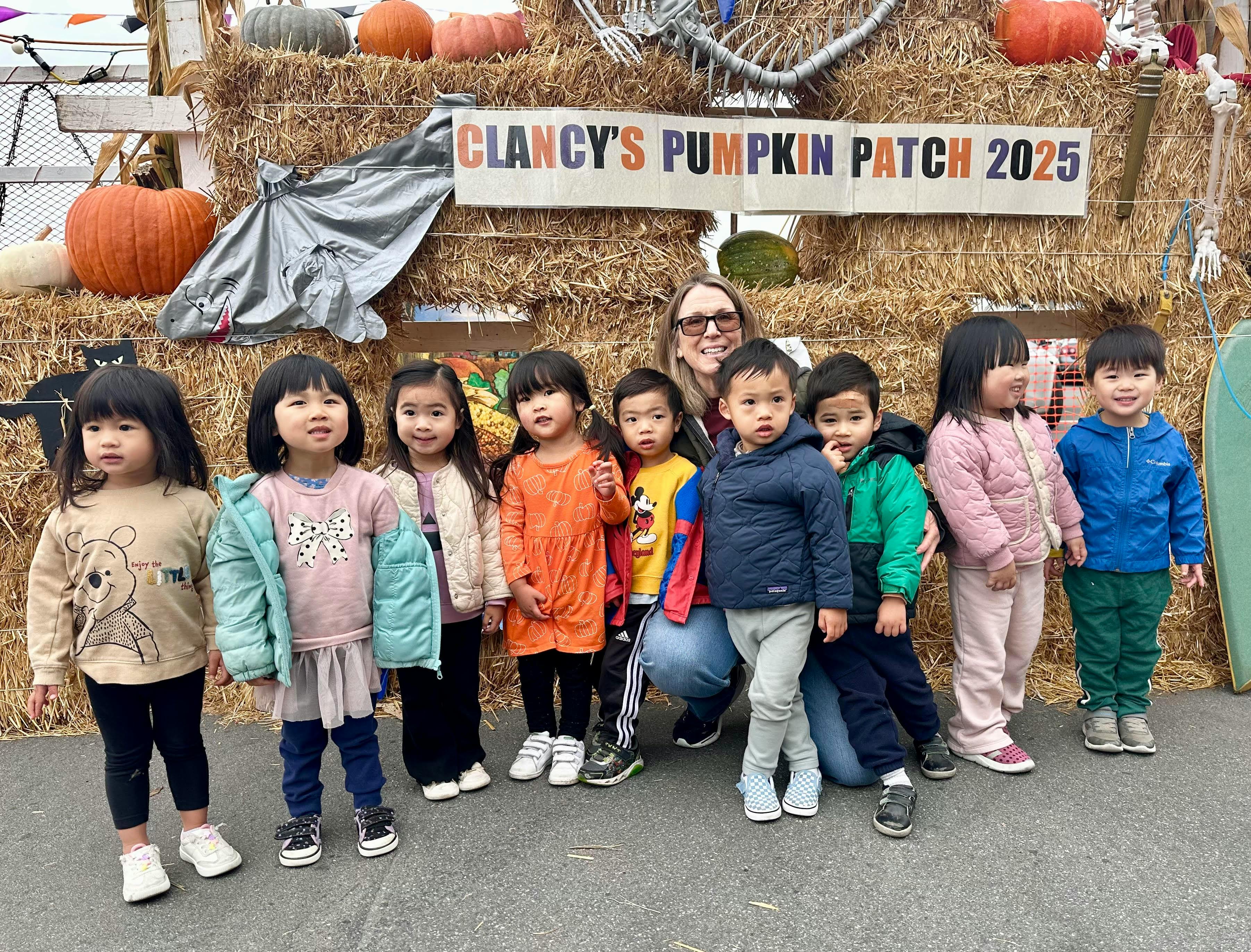 A person and children posing in front of Clancy's Pumpkin Patch sign