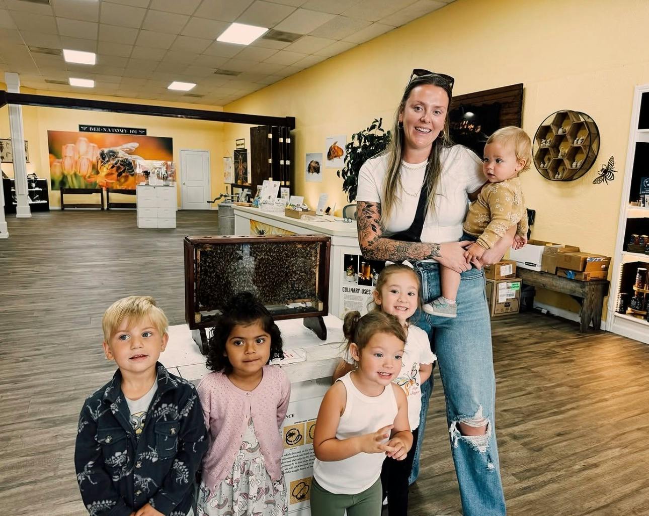 Adult and several children gathered near a bee observation hive in a shop