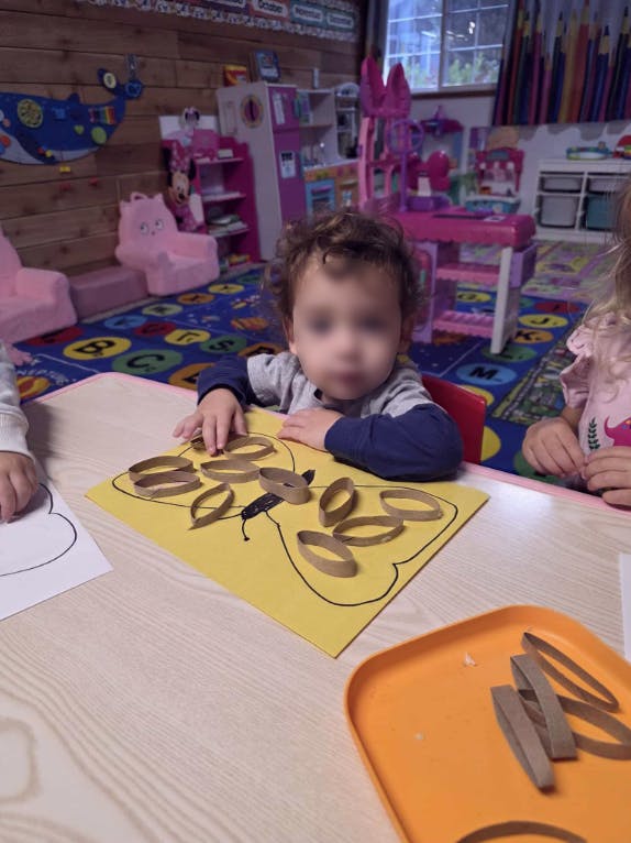 Child making a craft with paper rings on a yellow sheet in a classroom