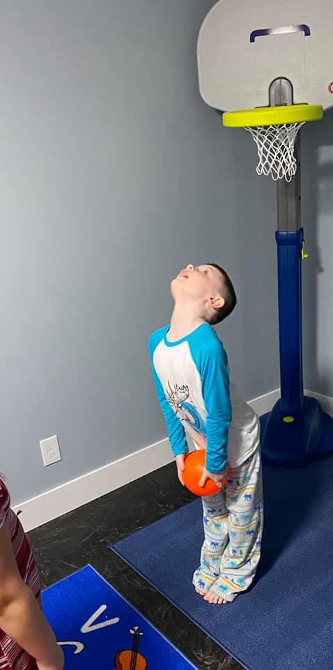 Child holding a ball and looking up at a basketball hoop