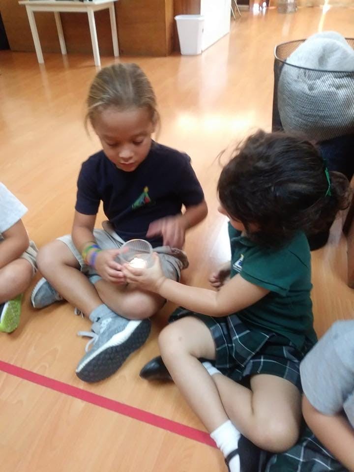Two children sitting on the floor holding a small container with a light inside