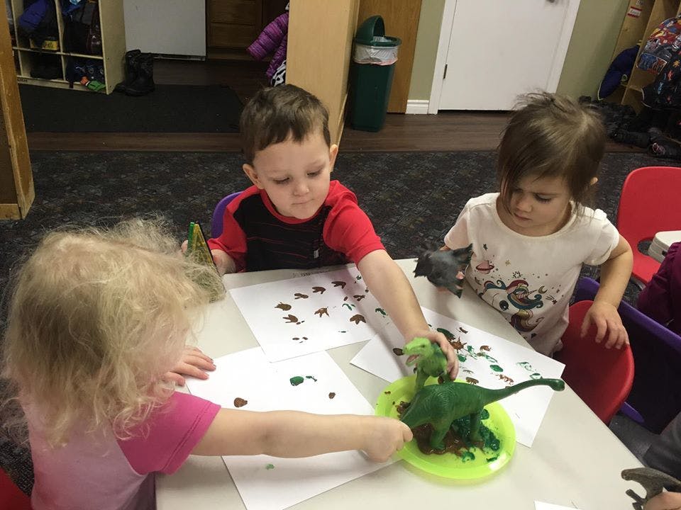 Three children playing with dinosaur toys and paint on paper