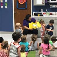 Adult reading a book to a group of children in a classroom