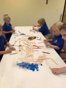 Children building with craft sticks and small blue blocks at a table