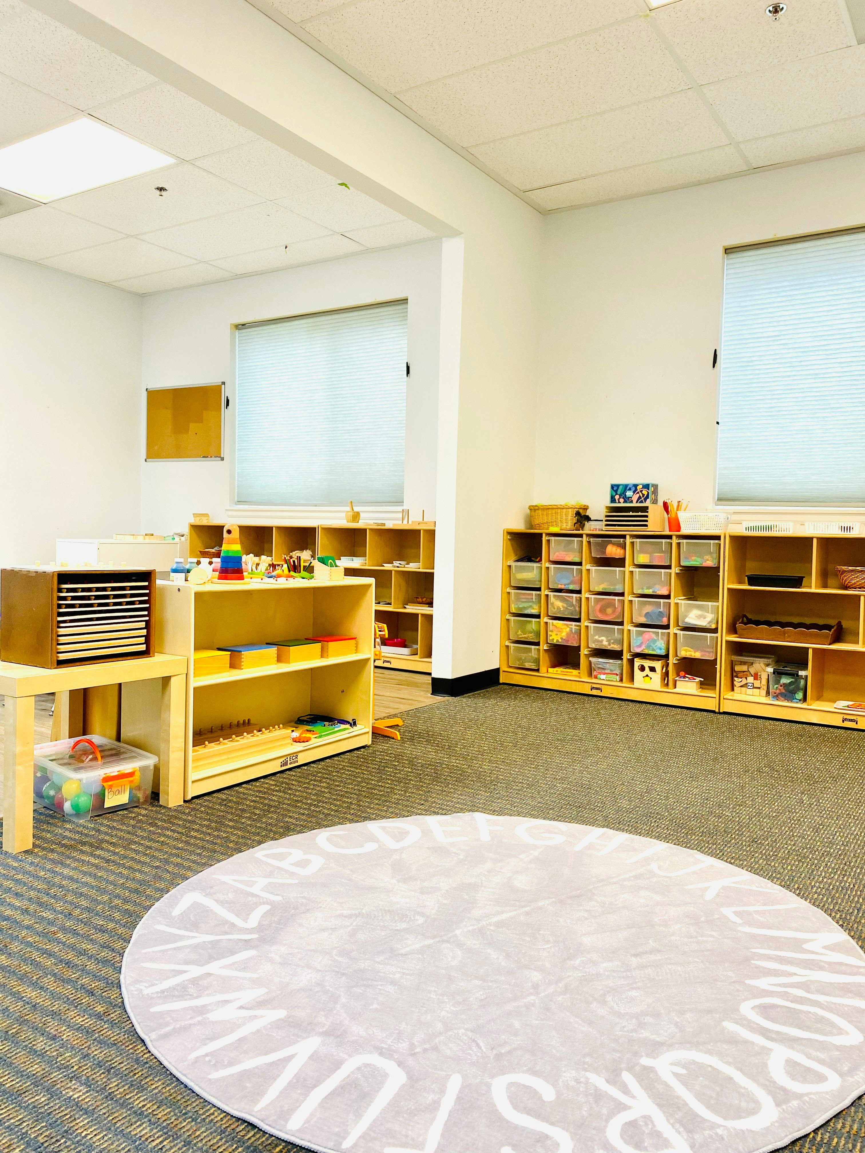 Classroom with shelves of learning materials and a round rug with letters