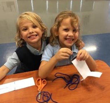 Two children at a table with scissors and string